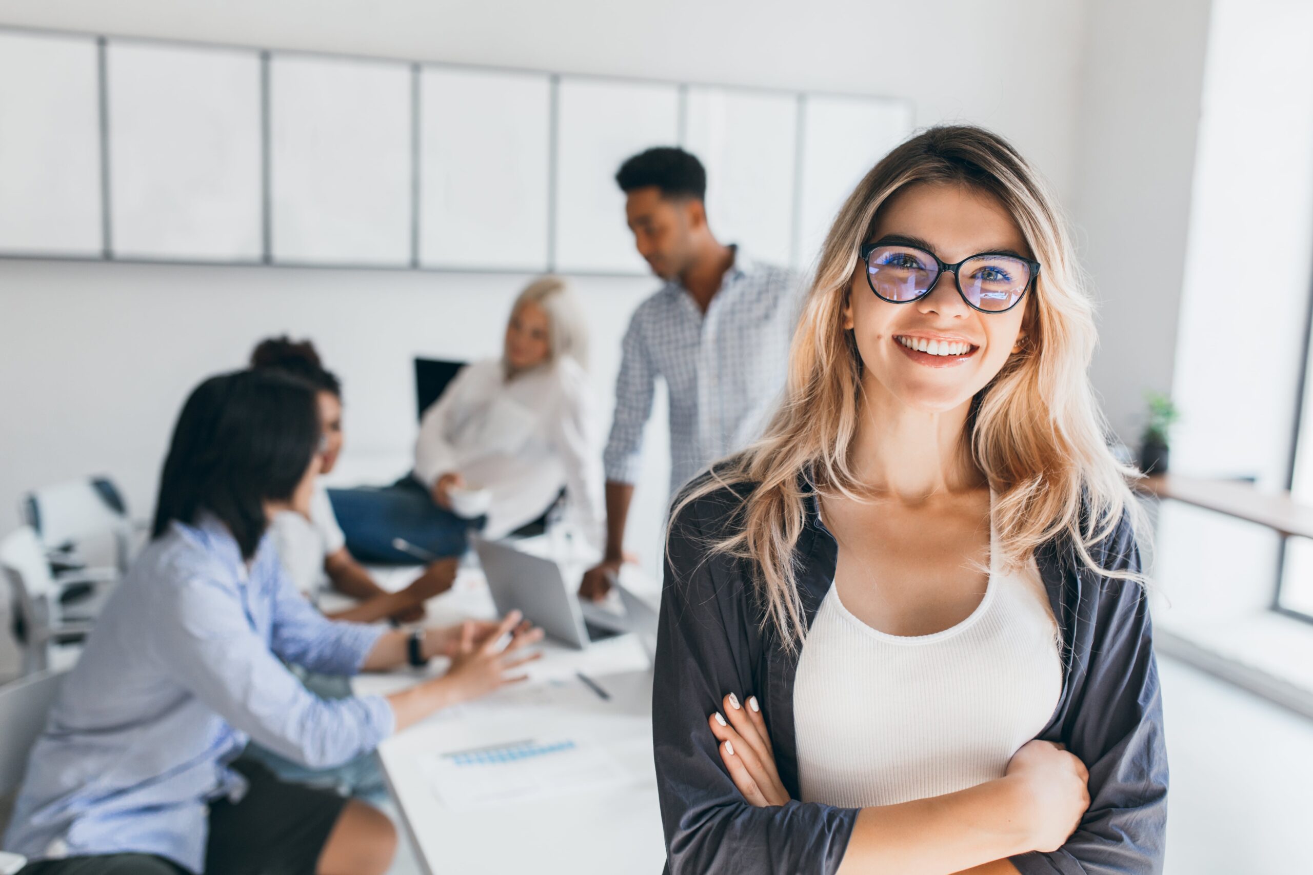 blonde-female-executive-posing-with-smile-arms-crossed-during-brainstorm-with-managers-indoor-portrait-european-student-spending-time-hall-with-asian-african-friends (1)-min